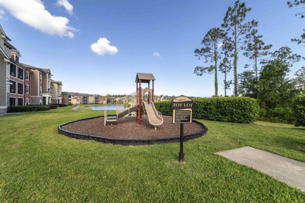 Integra Woods Small playground with slide and climbing set on mulch, beside a "Tot Lot" sign, near apartments and a lake.