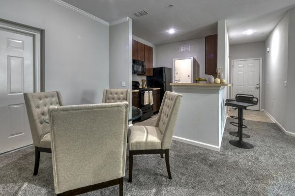 Integra Woods Modern kitchen and dining area with beige chairs, round glass table, and a breakfast bar with two black stools.