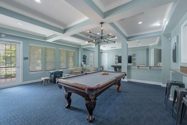 Integra Woods Modern game room with a pool table, foosball table, lounge chairs, and large windows with natural light.
