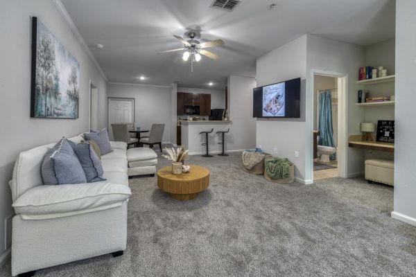 Integra Woods Modern living room with a white couch, coffee table, TV, open kitchen, dining area, and a glimpse of a bathroom and bedroom.