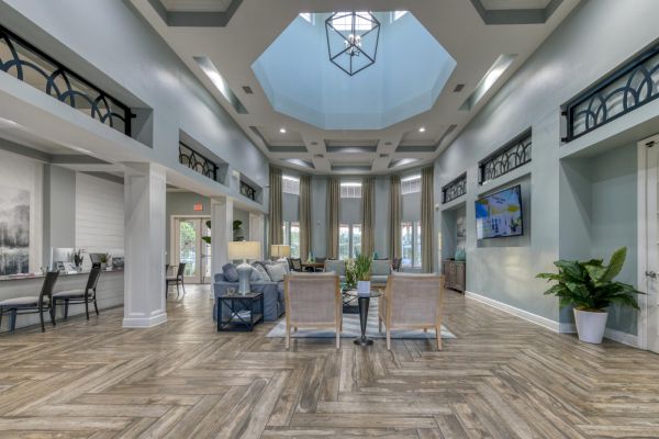 Integra Woods Spacious, modern lounge with tall ceilings, wood floors, skylight, and stylish seating arranged around a central table.