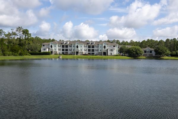 Integra Woods Apartment buildings and trees are reflected in a calm lake under a blue sky with white clouds.