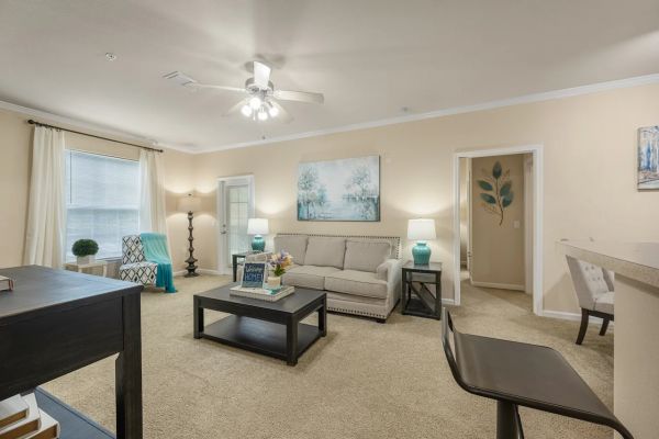 Integra Woods Bright living room with beige walls, tan carpet, a sofa, coffee table, and blue accent decor.