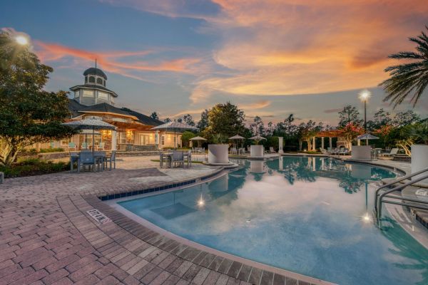 Integra Woods A resort-style pool with lounge chairs and umbrellas, surrounded by trees and a building at sunset.