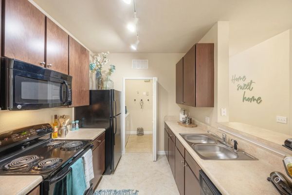 Integra Woods Modern galley kitchen with brown cabinets, black appliances, and a "Home Sweet Home" sign on the wall.