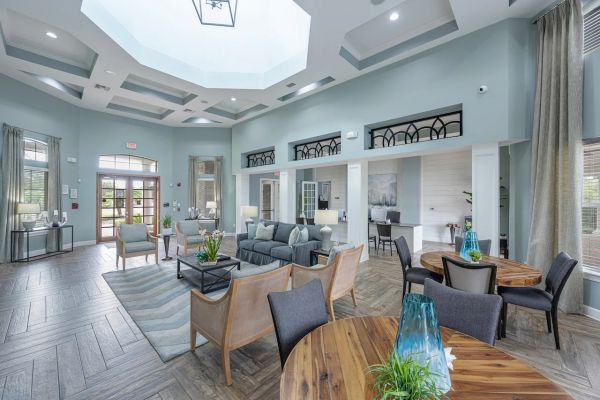 Integra Woods Spacious, modern lounge with sofas, round tables, wood floors, large skylight, and tall windows.