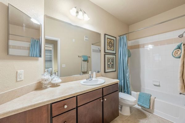 Integra Woods Modern bathroom with a large mirror, sink, brown cabinets, and a bathtub with blue towels and shower curtain.